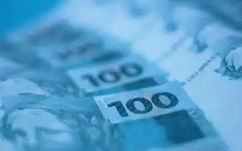 Notas de 100 reais em close, com tom azulado
